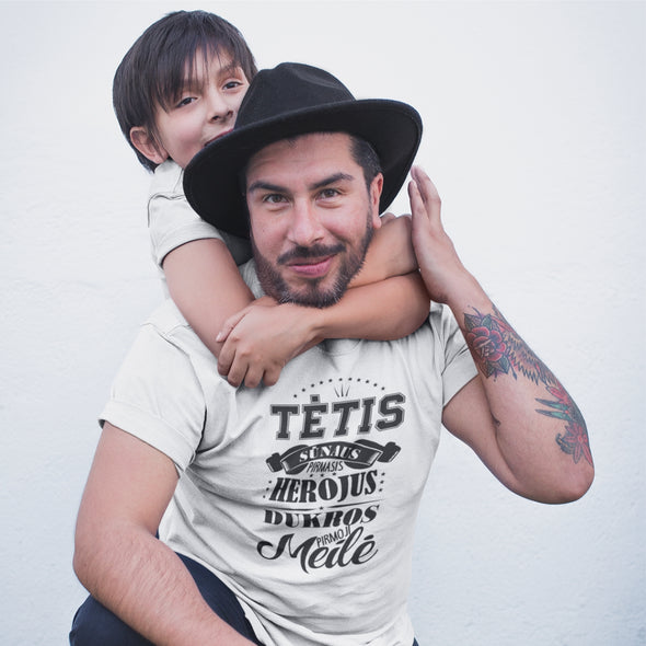 Balti marškinėliai su juodu užrašu "Tėtis herojus ir pirmoji meilė"